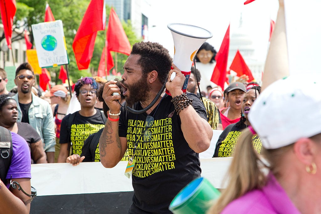 Black man speaks wearing a Black Lives Matters t-shirt rallies the crowd at Peoples Climate March