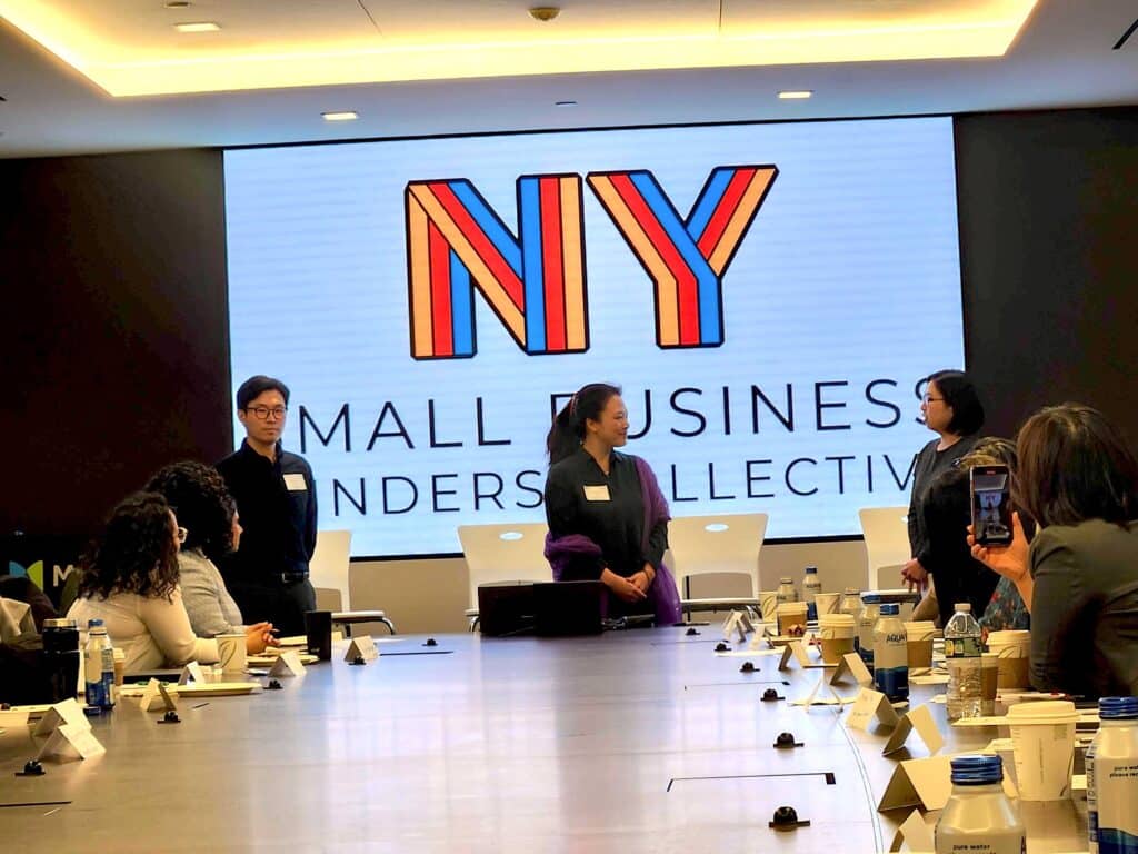 NY Small Business Funders Collective meeting. Asian American Federation representatives stand at the front of the table. 