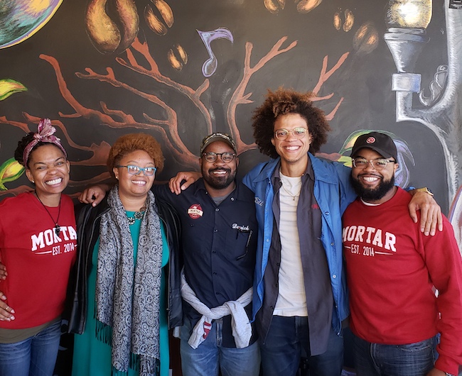 Five people stand arm in arm smiling