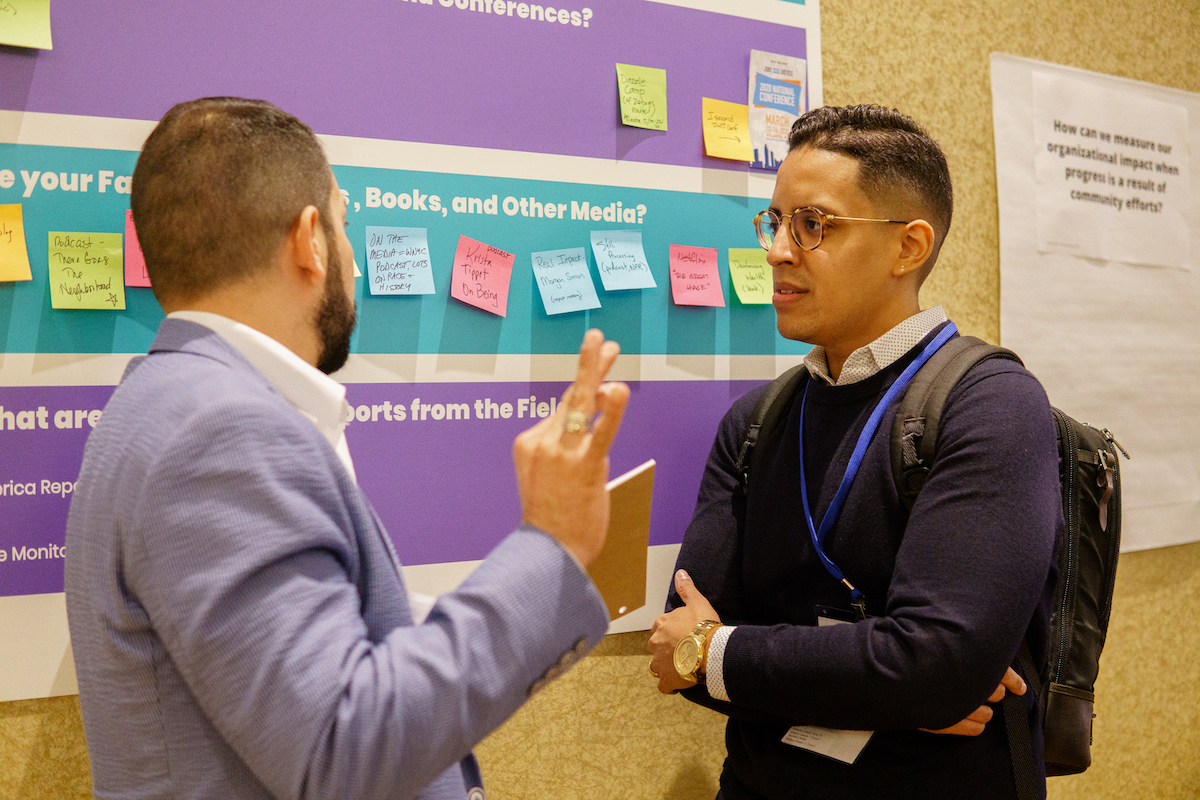 One person speaks to another person in front of a poster with post-it notes