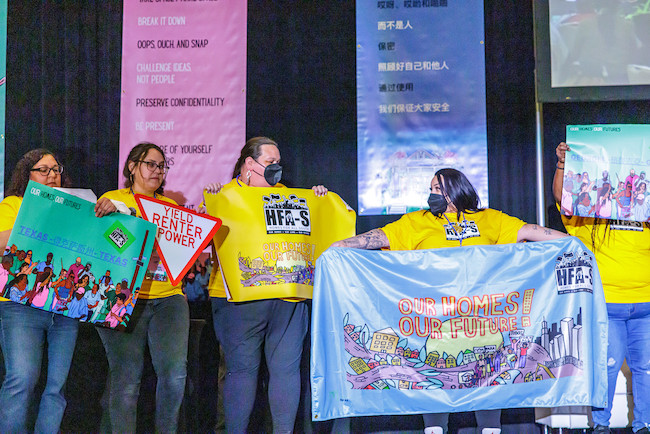 Five people stand on a stage holding banners that read 