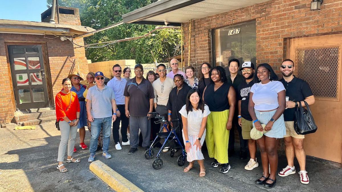 A group of twenty people stand and smile in front of two brick houses.