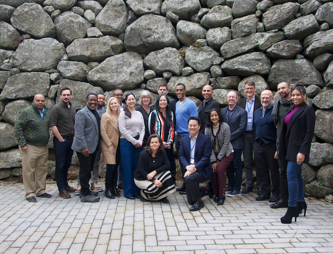 A group of people stand smiling in front of a wall of rocks