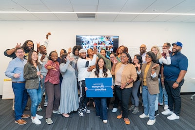 A group of people laugh and smile, holding a sign that reads, 