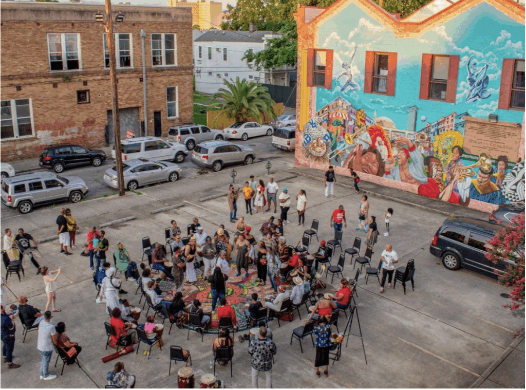 People gather in the Ahse Parking lot next to a vibrant mural of artists