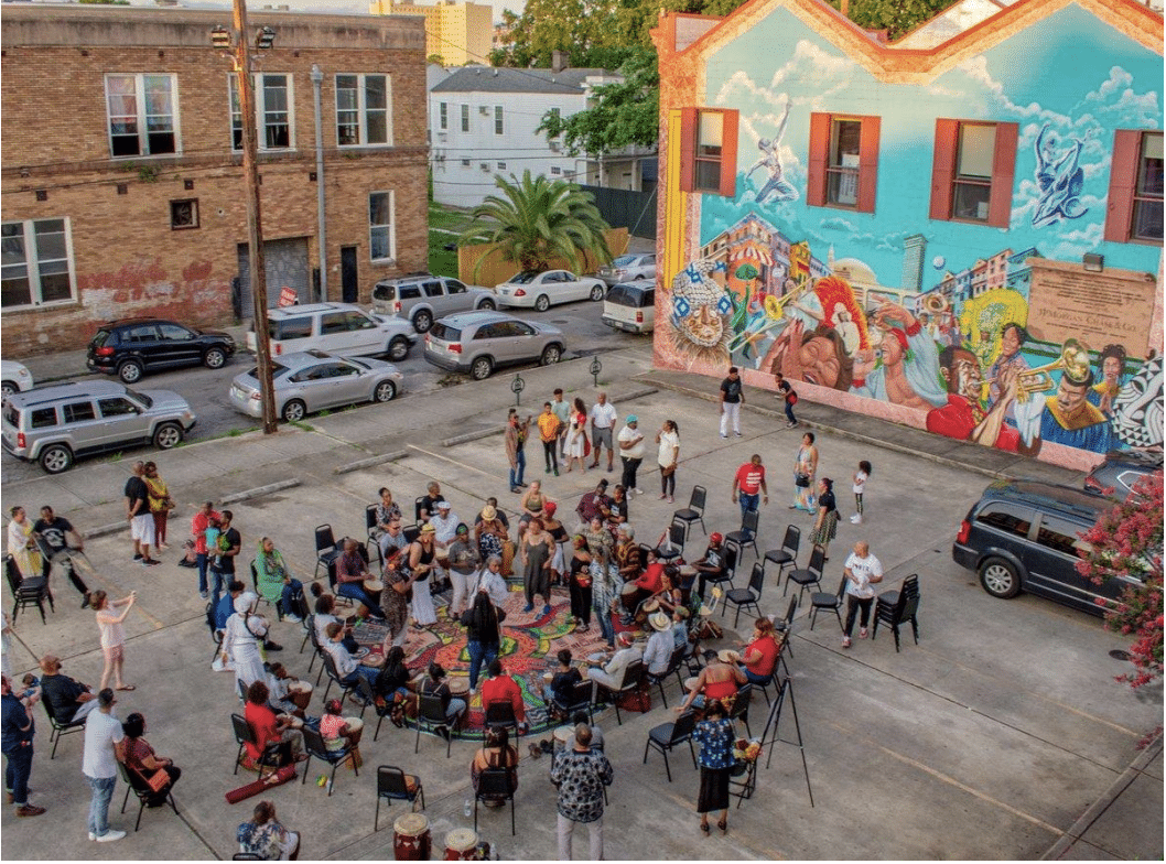 People gather in the Ahse Parking lot next to a vibrant mural of artists